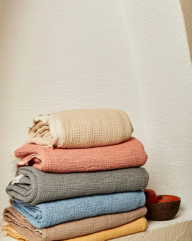 Folded muslin blankets in cream, coral, grey, blue, brown and yellow