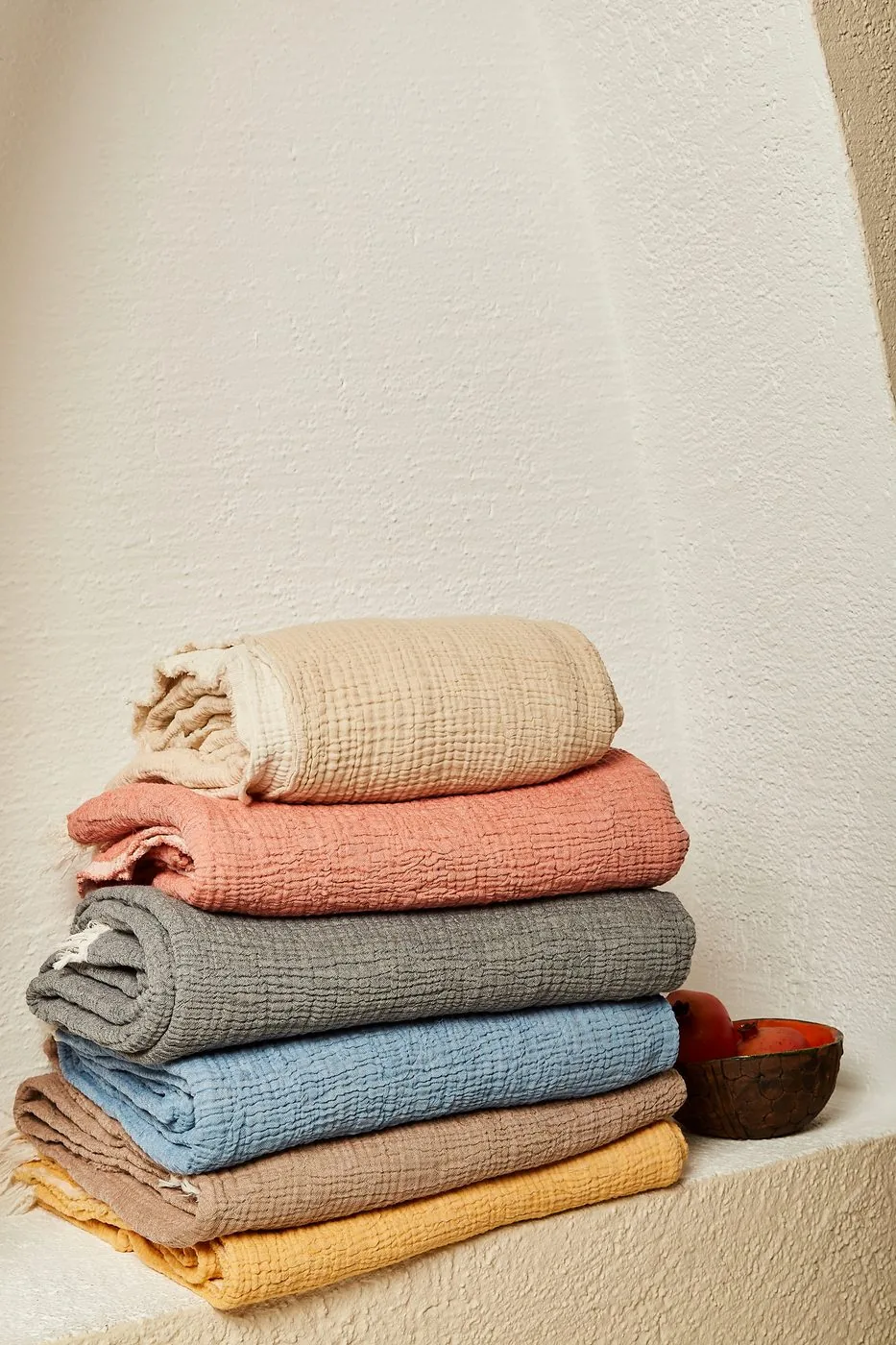 Folded muslin blankets in cream, coral, grey, blue, brown and yellow
